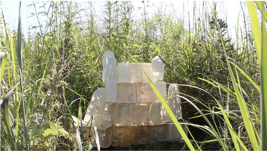 A stack of white bricks made out of paper sits among tall prairie grasses