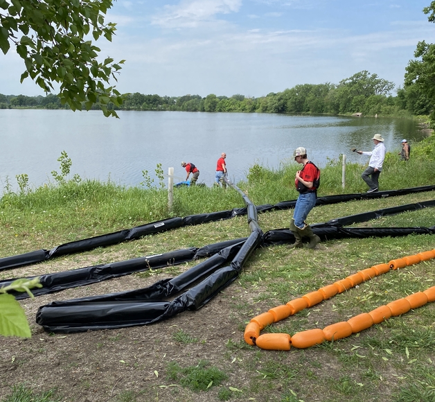 A team in red shirts pull lengths of black and orange rubber tubing out into a lake