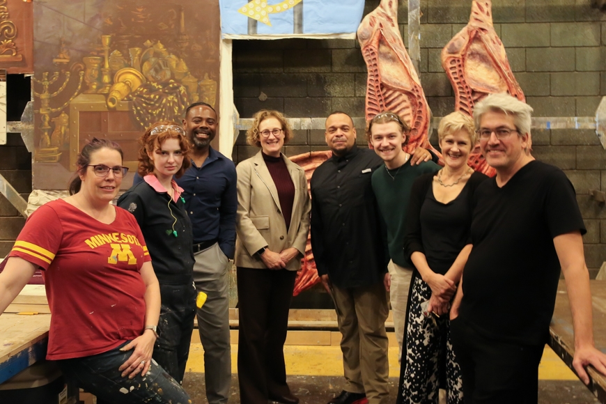 a group of faculty, staff, & students pose in front of several theatre set pieces