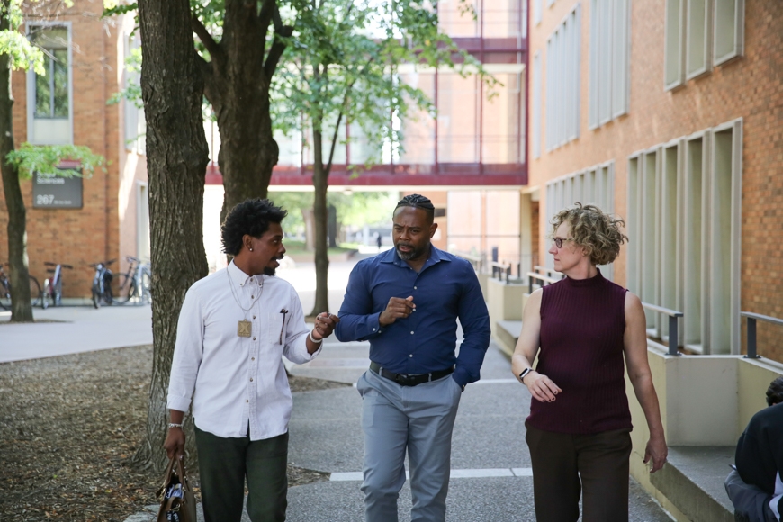 three faculty members walk and talk together outside