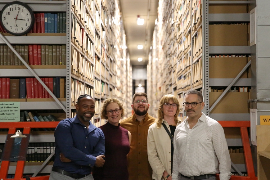 a group poses in front of stacks in a library archive