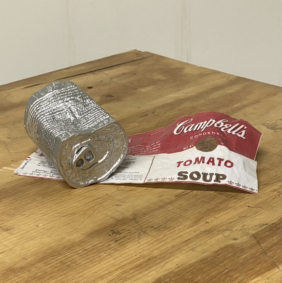 A slightly crushed silver can lays on its side atop a Campbell’s Tomato Soup label.