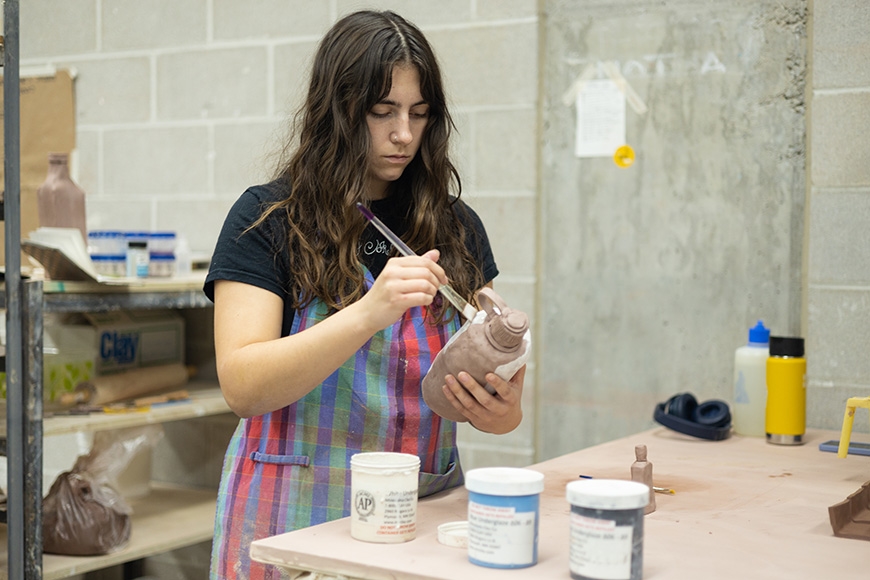 Student in a striped apron focused on painting their project
