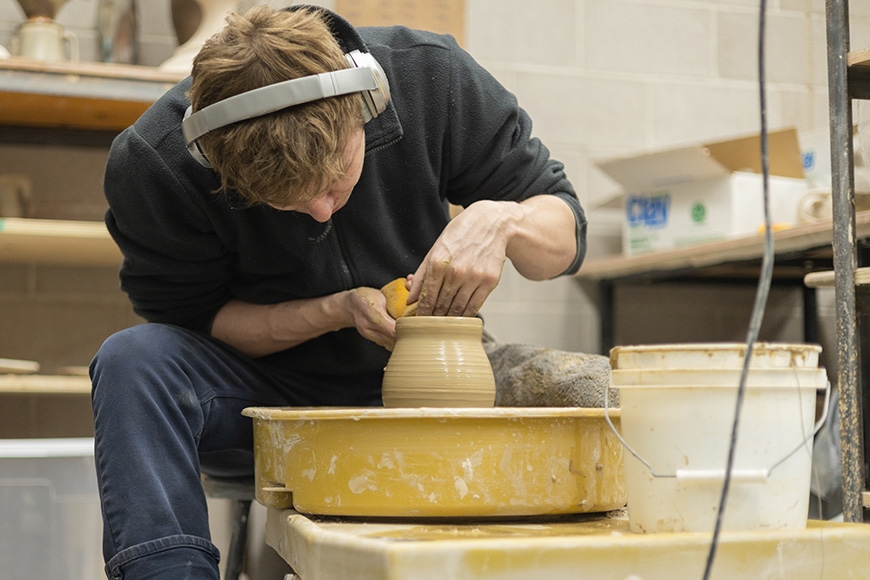 Student listens to music while shaping their project on the pottery wheel