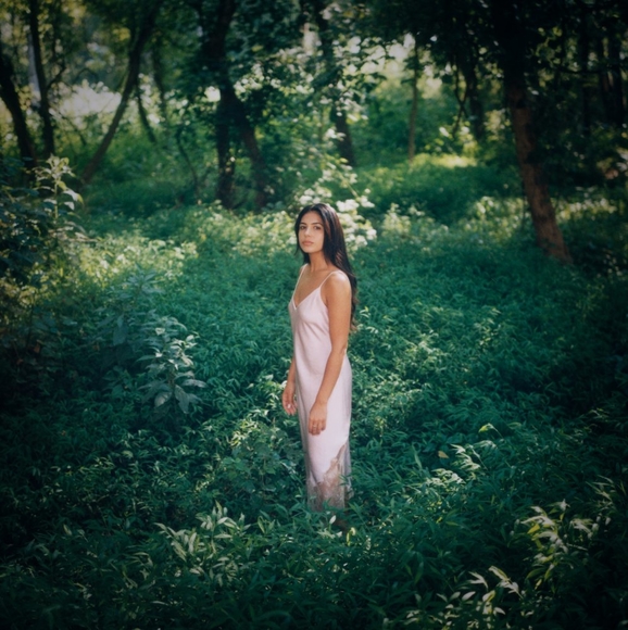 A woman in a pink satin dress stands in a lush green forest