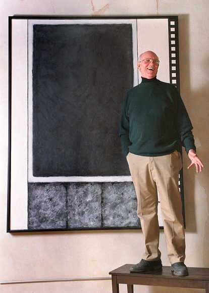 Dr. Harold Adams stands on a table talking in front of a six foot tall abstract painting