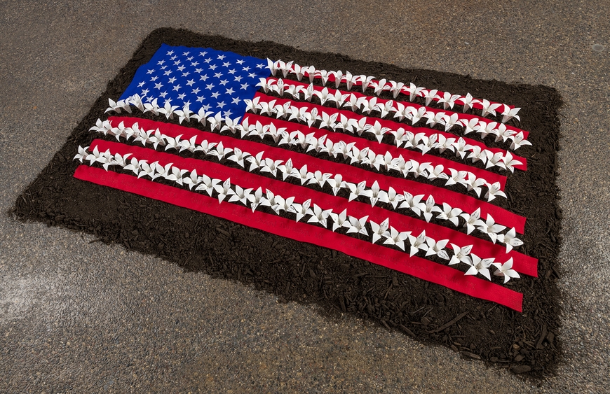 American flag made of origami flowers on a pile of dirt on concrete floor