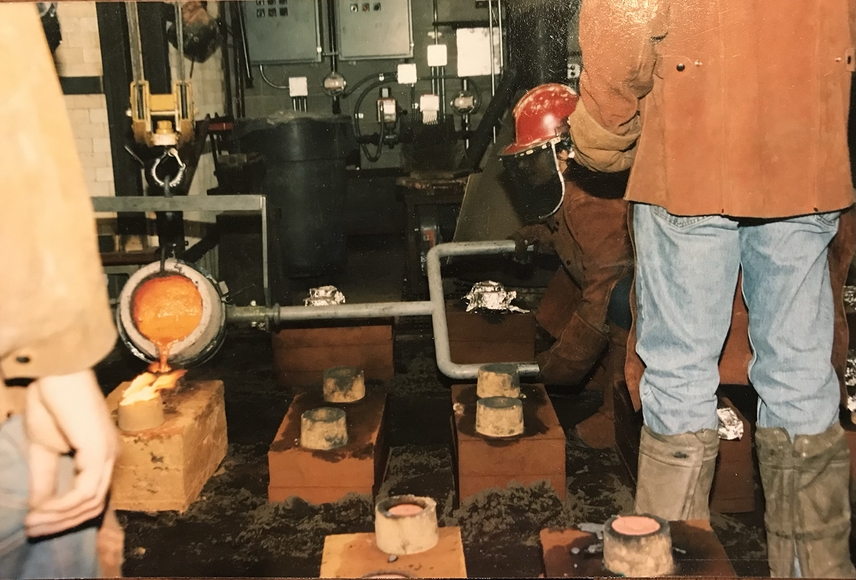 Students in protective gear pour metal in a foundry