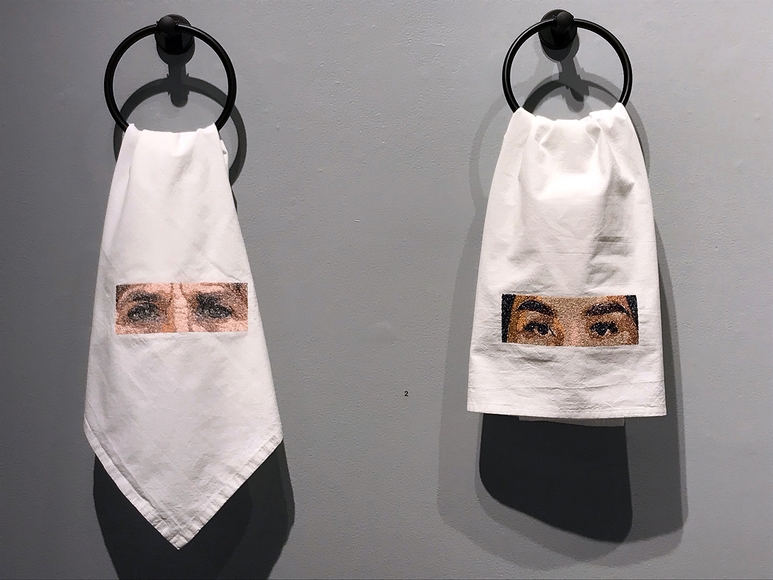 Eyes embroidered onto hand towels hanging on a gray wall
