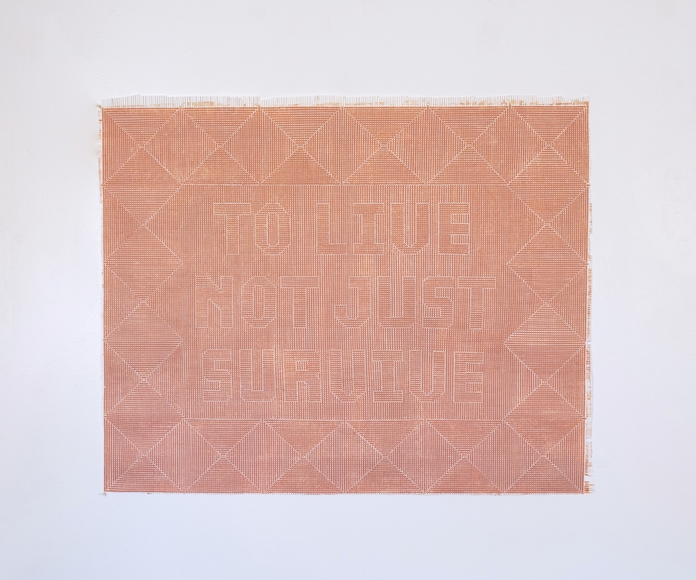 Orange and white textile artwork that reads "TO LIVE NOT JUST SURVIVE"