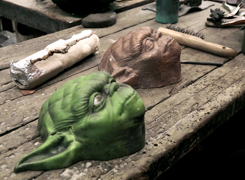 A green Yoda mask and a bronze cast of it sit on a workbench next to a lightsaber-shaped mold