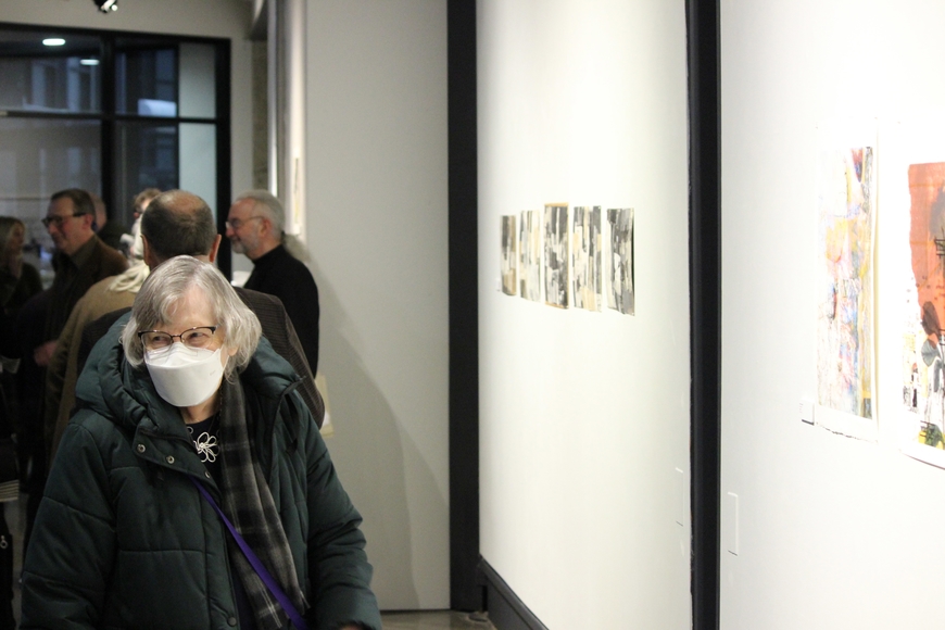 An elderly woman in a white mask enters an art gallery