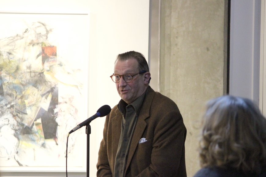 A man speaks into a microphone in front of abstract artwork