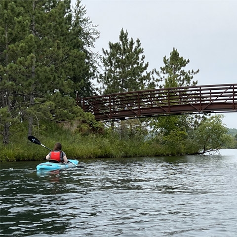 Hannah Ward kayaks in a river near a wooden bridge