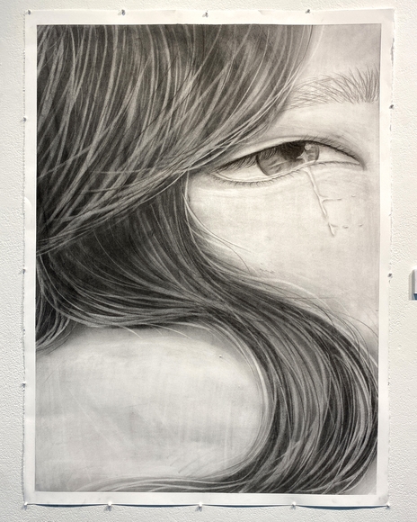 Charcoal drawing of a close up on a person's hair and their eye shedding a tear