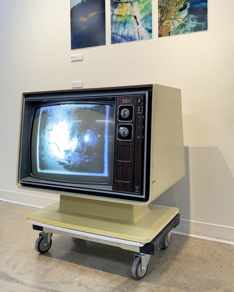 Vintage tube television on a dolly playing a black and white grainy video underneath three photos tacked to the wall
