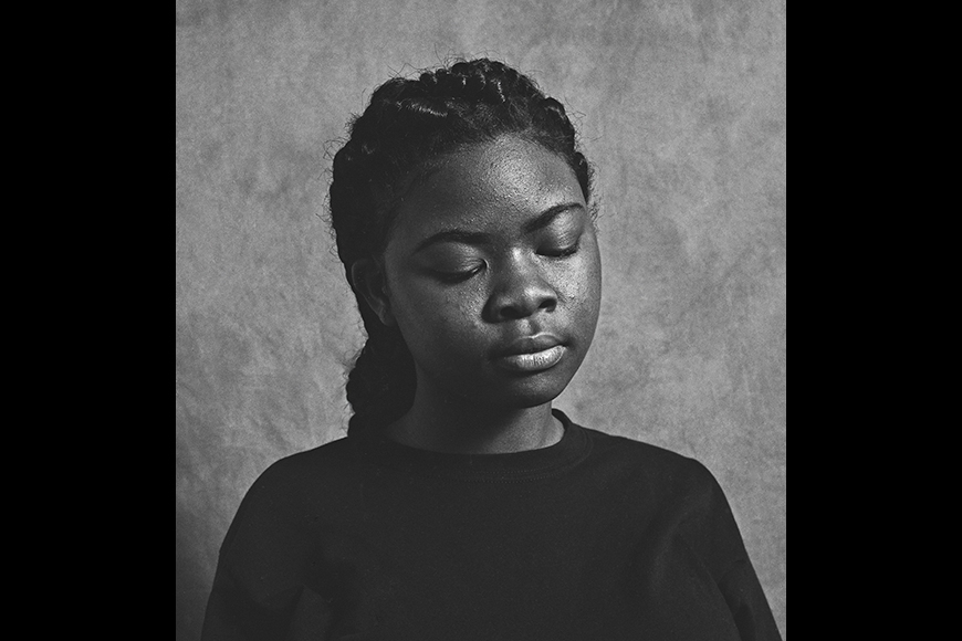 Photograph of a Black young women with eyes closed and a serene expression as she faces the camera.