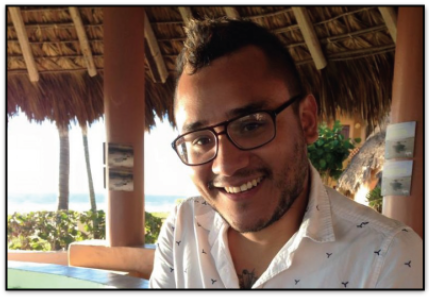 Jesus Estrada-Perez in white shirt with black glasses smiling under a tiki hut