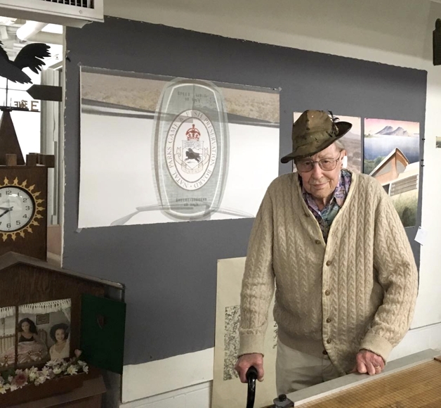 Elderly man in hat and sweater stands in an art studio