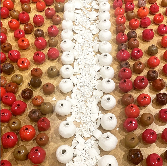 Multiple rows of red and white ceramic pomegranates on the floor, the center row crushed into shards