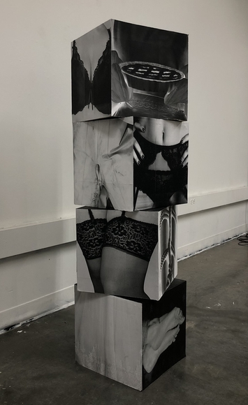 A set of four stack cubes covered in cropped photographs of areas of women’s bodies such as legs, torsos, and chests.
