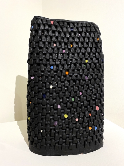 Black woven ceramic sculpture interspersed with multi-colored beads, standing on a pedestal
