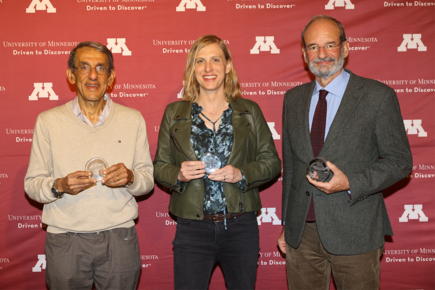 Dr. Joseph Ibrahim, Dr. Carrie Strief, and Dr. Piercesare Secchi hold their alumni awards and stand in front of a maroon U of M backdrop for photos
