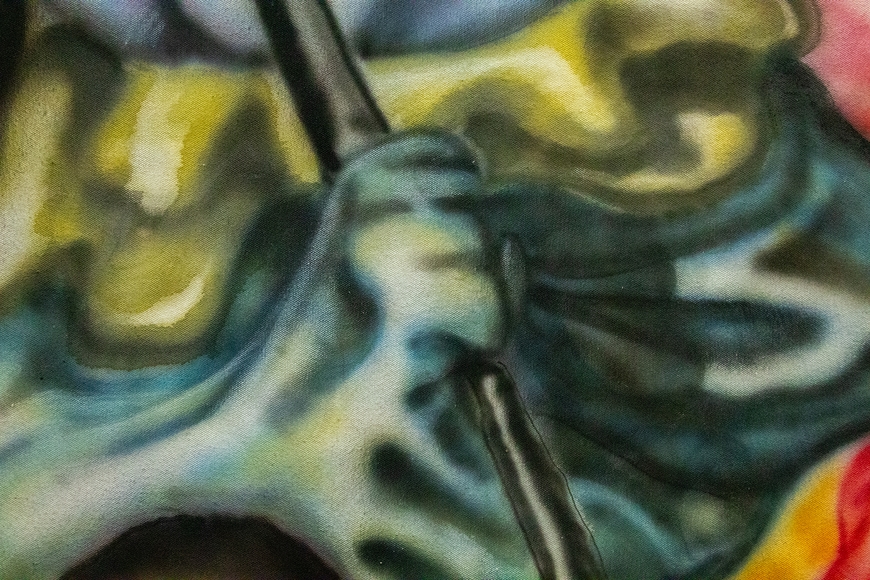 A hand, covered in a sickly green cloth with gold fringe, grasps a metallic pole.
