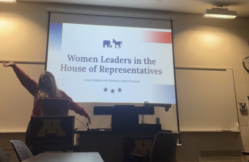 Kristin standing in front of projected screen, with PowerPoint slide text reading "Women Leaders in the House of Representatives"