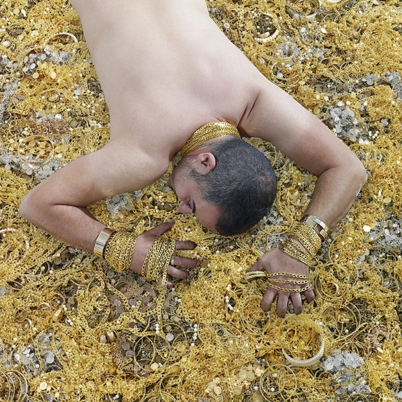 Man laying face down in a pile of gold jewelry