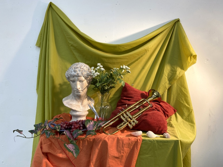 Still life display with bust, flowers, and trumpet on green and orange fabrics