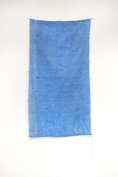 A tattered blue rectangle of fabric hangs on a white wall