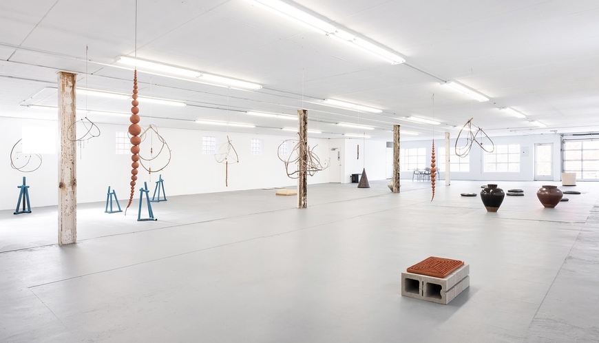 Bright warehouse sized art gallery displaying multiple sculptures sitting on the floor and hanging from the ceiling