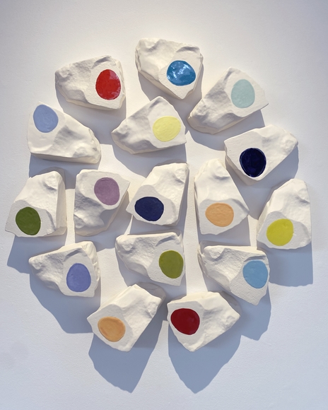 White blocks with colored circles hang in a circle on a white wall