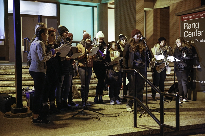 Group of 13 students sing outside Rarig Center. They are part of The Enchantments acapella group.