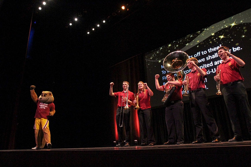 Goldy and a group of 5 brass instrument musicians on Northrop stage