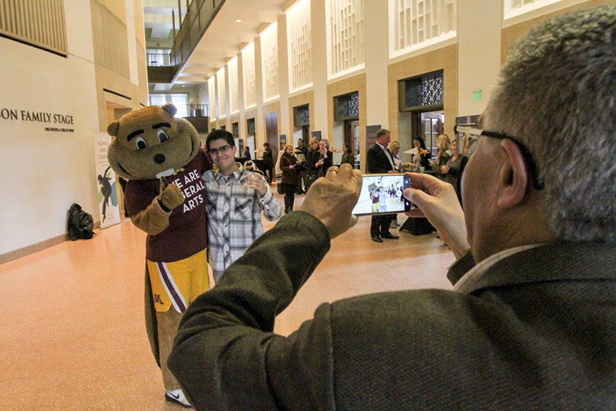 Photo of a parent taking a photo of a young man posing with Goldy Gopher
