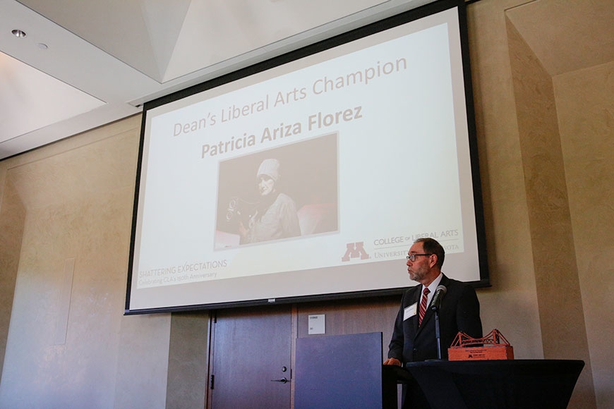 John Coleman stands near a photo of Patricia Ariza Florez, who won the Dean's Liberal Arts Champion Award