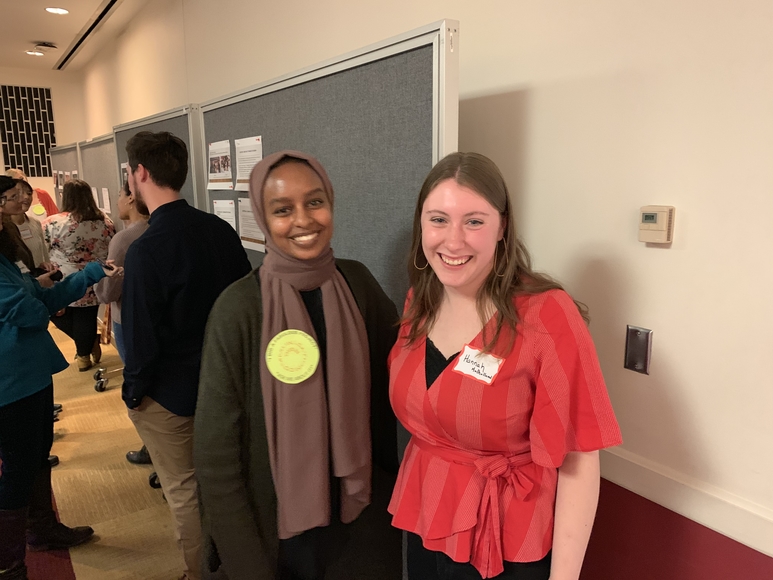 Saharla Afkarshe, Hannah Mulholland pose while other students discuss their presentations to onlookers in the background