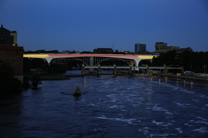 Looking over Mississippi toward 35W bridge, lighted in maroon and gold, University of Minnesota buildings in the background