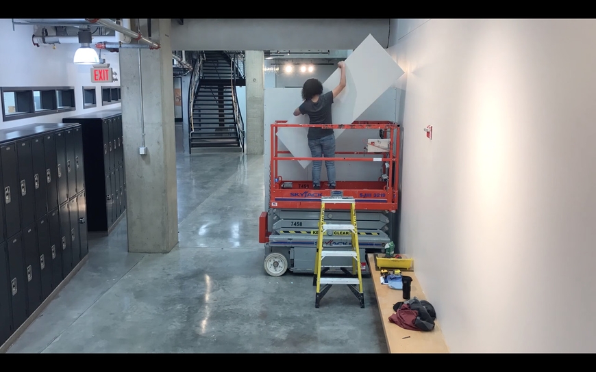 Artist working on a scissor lift in the Regis Center installing drywall panels 