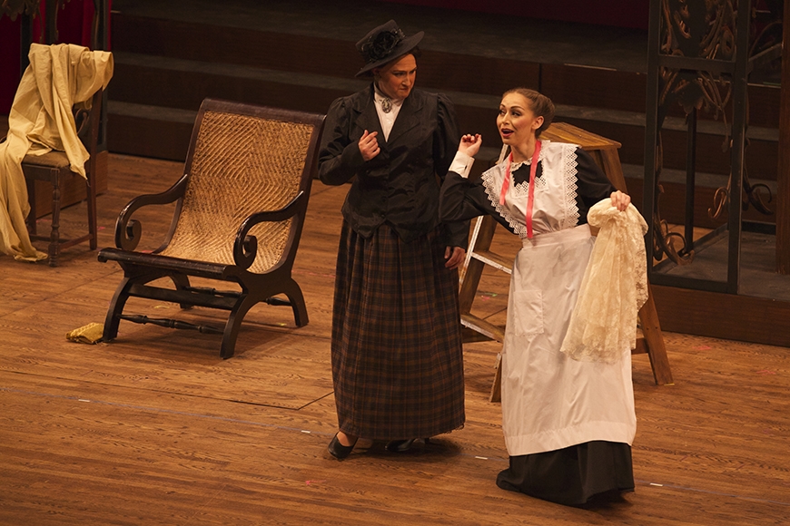 Woman dressed as a maid singing with an elderly woman in Victorian dress