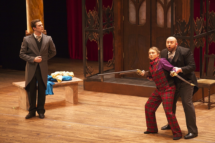 A woman holding a gun and a sword with two men in suits next to her
