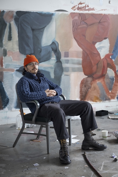 White man in orange cap sits in an art studio