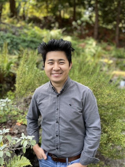 A photo of Yuyang Zhao, smiling and wearing a grey button up in front of nature