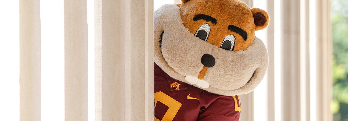 Goldy Gopher peering out from behind column