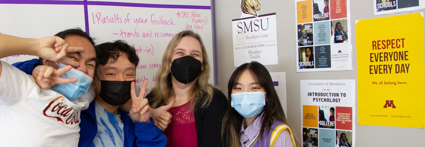 Three students and a teacher smiling at the camera with posters in the background
