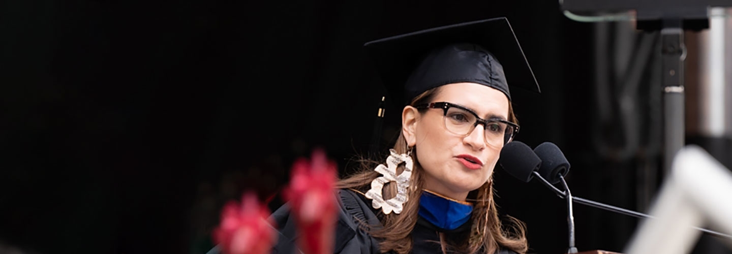 Peggy Flanagan in a mortarboard speaking at a podium at commencement