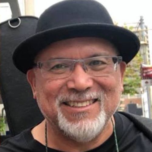 Professor Vicente Diaz, a person with a grey beard and mustache and glasses, wearing a black hat and smiling.