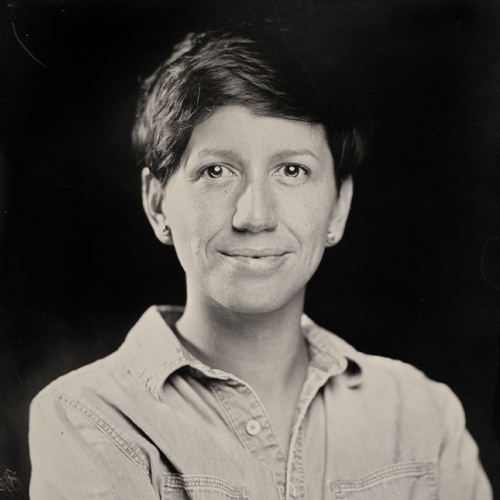 Black and white tintype portrait of a woman with arms folded and smizing
